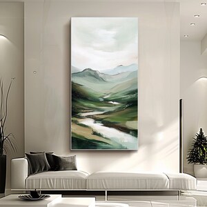 May include: Vertical landscape painting depicting a serene valley with rolling green hills, a winding river, and a soft, cloudy sky. The artwork uses a palette of greens, blues, and whites, creating a calming and natural aesthetic. The painting is displayed in a modern living room setting.