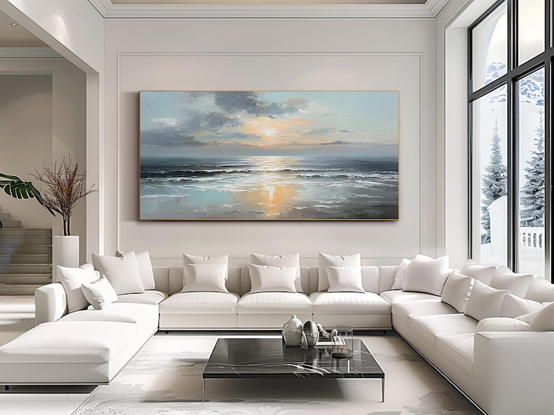 Op de afbeelding: Groot rechthoekig olieverfschilderij dat een zeegezicht met zonsondergang uitbeeldt. Het kunstwerk heeft een palet van blauw, grijs en geel, met de zon die reflecteert op het water. Het schilderij hangt boven een witte hoekbank in een moderne woonkamer.