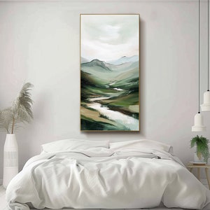 May include: Vertical landscape painting featuring a valley with a river winding through green and brown hills. The artwork has a gold frame and is displayed above a bed with white linens. The color palette includes shades of green, brown, and white.