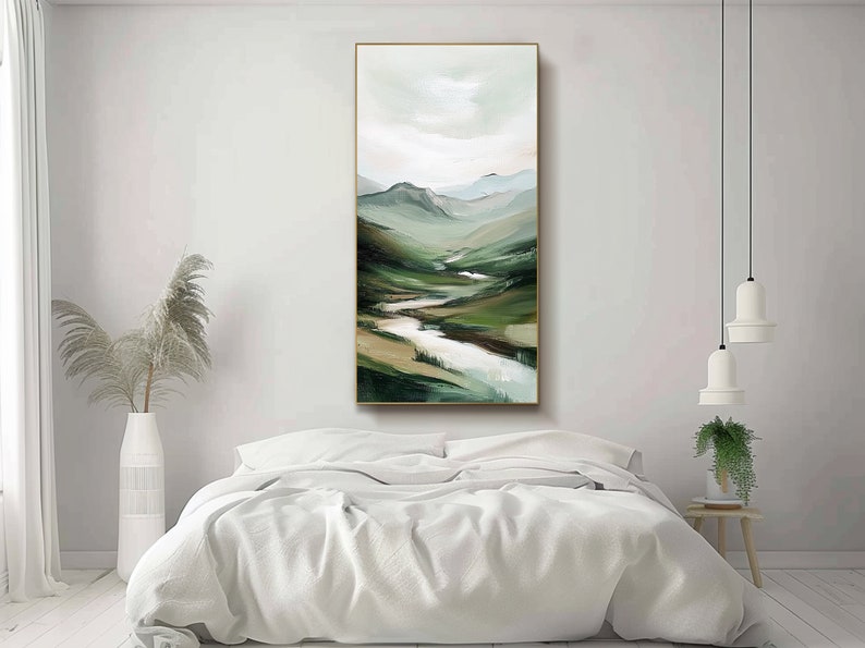 May include: Vertical landscape painting featuring a valley with a river winding through green and brown hills. The artwork has a gold frame and is displayed above a bed with white linens. The color palette includes shades of green, brown, and white.