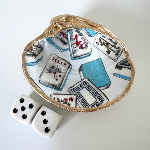 May include: A decorative oyster shell bowl with a gold rim, featuring a playing card design. Two white dice with black dots are next to the bowl. The bowl's interior has a light blue background with playing card illustrations.