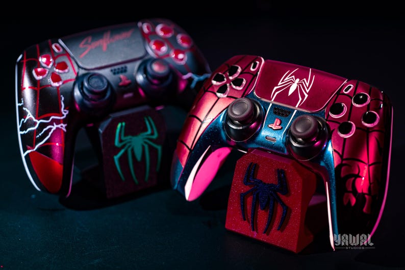 May include: Two custom-designed game controllers with matching stands. The controllers feature a red and black color scheme with spiderweb and lightning bolt designs. The stands have a spider logo. The word "Sunflower" is visible on one controller.