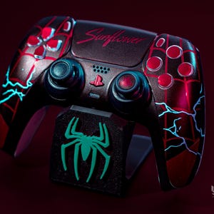 Könnte beinhalten: Benutzerdefinierter schwarzer und roter Videospiel-Controller mit Spider-Man-Motiv. Der Controller hat rote Knöpfe, blaue Akzente und das Wort "Sunflower". Ein passender Ständer mit grünem Spinnenlogo ist im Lieferumfang enthalten.