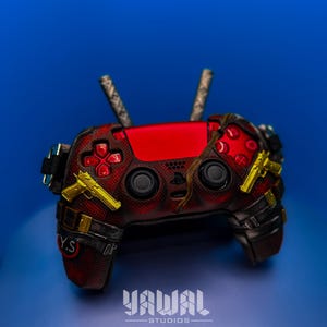 May include: A red and black custom PlayStation 4 controller with gold accents. The controller has a textured design and features a custom grip. The controller is on a blue background.