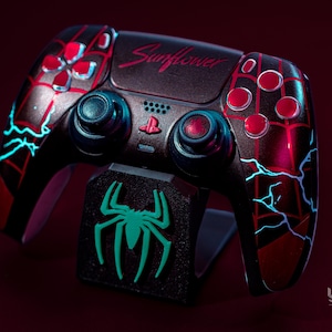 May include: Custom black and red video game controller with a Spider-Man theme. The controller features red buttons, blue accents, and the word "Sunflower". A matching stand with a green spider logo is included.