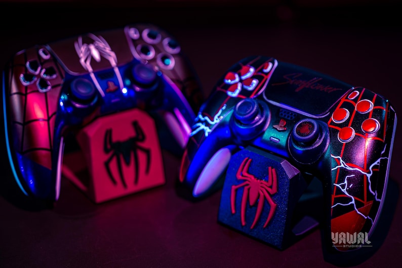 May include: Two custom-painted game controllers with matching stands. The controllers feature a Spider-Man theme with red, black, and blue accents. One controller has the text "Skyflower". The stands display a red spider logo.