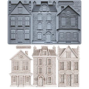 May include: A gray silicone mold featuring three distinct house designs with brick and siding textures, labeled Old Colchester Road. Below the mold are three casted house figures in a light beige finish, matching the designs of the mold above.