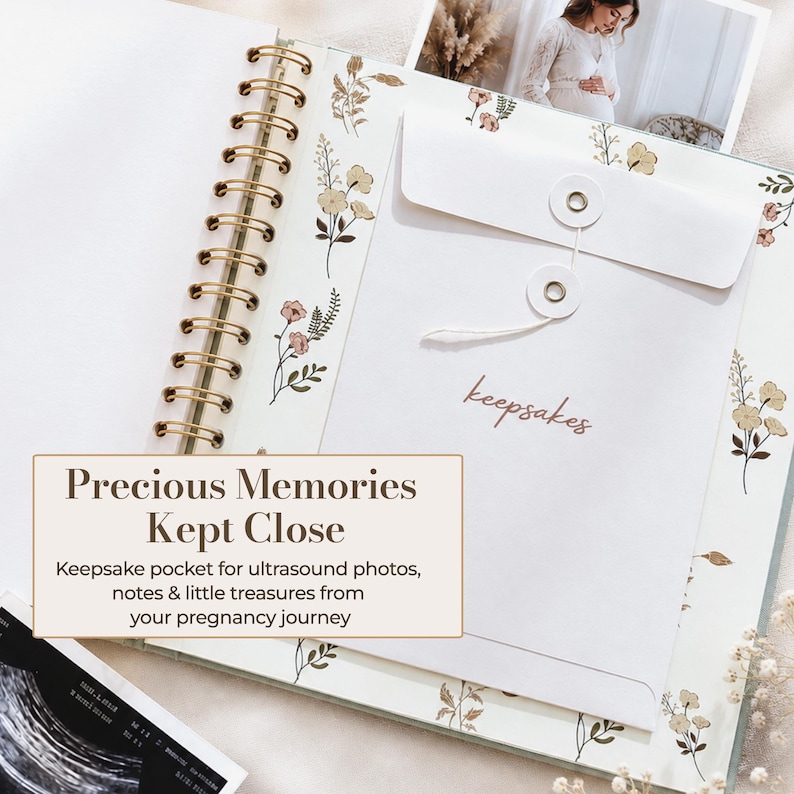 May include: A spiral-bound scrapbook featuring a floral pattern on the pages and a white envelope with a string-tie closure labelled "keepsakes" in cursive script. The book includes a pocket for storing ultrasound photos and small mementos.