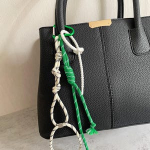 May include: Black leather tote bag with a white and green rope keychain. The keychain has a white plastic ring and a green plastic ring.