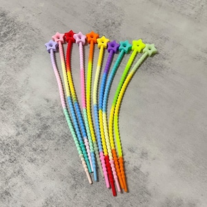 Puede incluir: Diez abalorios de cordones coloridos con tapas en forma de estrella. Los abalorios están hechos de silicona y tienen un diseño de color degradado. Los colores incluyen rosa, rojo, naranja, amarillo, verde, azul, morado y azul claro.