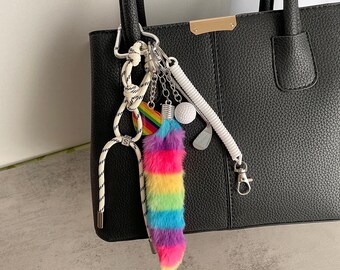 May include: A black leather tote bag with a rainbow fur keychain attached to the handle. The keychain also includes a golf ball, golf club, and a white rope.