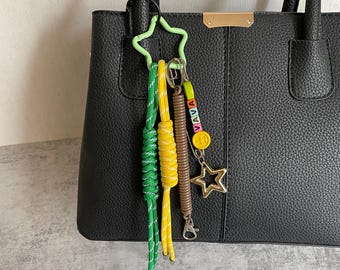 May include: A black leather handbag with a star-shaped keychain. The keychain has green, yellow and brown cords with a metal charm that says "VAVA".