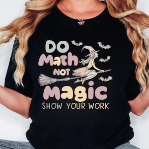 May include: Black t-shirt with a witch flying on a broomstick and the text "Do Math Not Magic Show Your Work" in colorful, rounded letters.