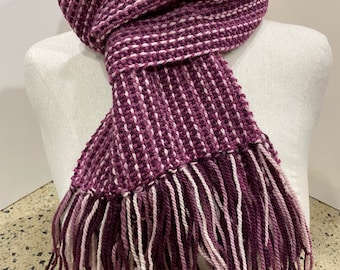 May include: A purple and white striped scarf with fringe on the ends. The scarf is tied around a white mannequin's neck.