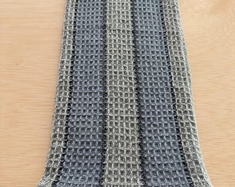 May include: A folded, rectangular kitchen towel with a waffle weave pattern. The towel features vertical stripes in shades of gray and blue. The bottom edge has a folded hem with a darker blue stripe.