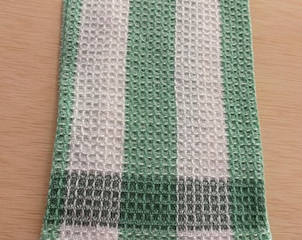 May include: A folded green and white striped kitchen towel. The towel has a textured, waffle-weave pattern. The stripes alternate between white and a light green color. A darker green band is at the bottom.