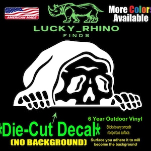 May include: A white die-cut decal featuring a skull design with a hood, hands, and the text "LUCKY_RHINO FINDS". The decal is made of 6-year outdoor vinyl and is American made. The decal has no background and sticks to any smooth, nonporous surface.