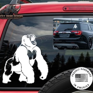 May include: White gorilla decal with open mouth, applied to a red vehicle window. The decal is next to a smaller image of a black SUV. The text "Lucky Rhino Designs" is visible. A sticker reads "Proudly Handmade in America."