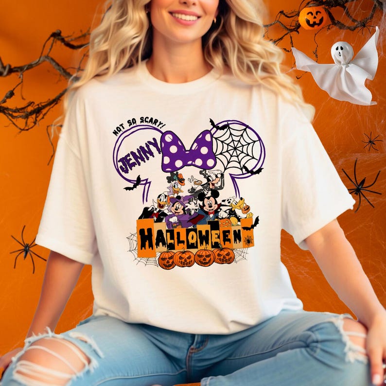 May include: White t-shirt with a purple and white Minnie Mouse ears design. The ears have a spiderweb and the text "Not So Scary! Jenny" inside. The design also includes Mickey Mouse, Donald Duck, Goofy, and Pluto characters with the text "Halloween" and pumpkins.