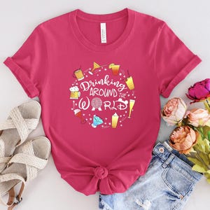May include: Pink t-shirt with a graphic of drinks and the text "Drinking Around the World" with a Disney World icon.