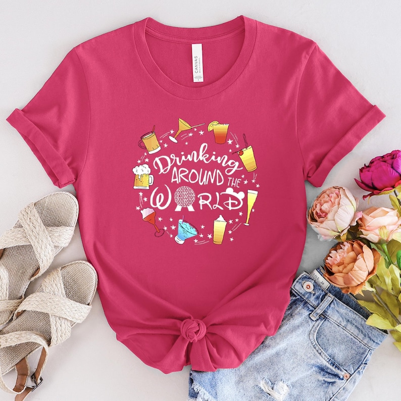 May include: Pink t-shirt with a graphic of drinks and the text "Drinking Around the World" with a Disney World icon.