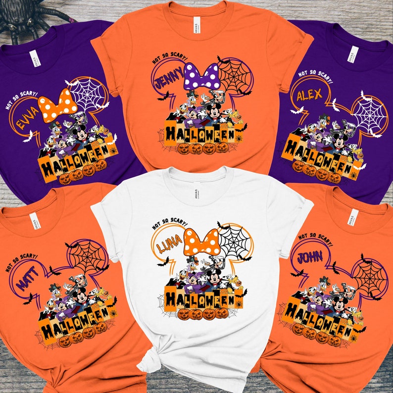 May include: Five orange, white, and purple t-shirts with a Mickey Mouse ear design. Each shirt has a different name on it, including "Eva", "Jenny", "Alex", "Matt", and "John". The shirts also have the text "Not So Scary!" and "Halloween" on them.