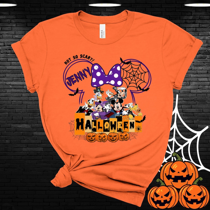 May include: Orange t-shirt with a Mickey Mouse Halloween design. The design features Mickey Mouse, Minnie Mouse, Donald Duck, Goofy, and Pluto. The text on the shirt says "Not So Scary! Jenny Halloween".