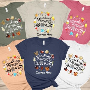May include: Six different t-shirts with various colors and designs. Each shirt features a circle with the text "Snacking Around the World" or "Drinking Around the World" and various Disney-themed icons. The shirts are available in colors such as white, light blue, pink, green, and beige.