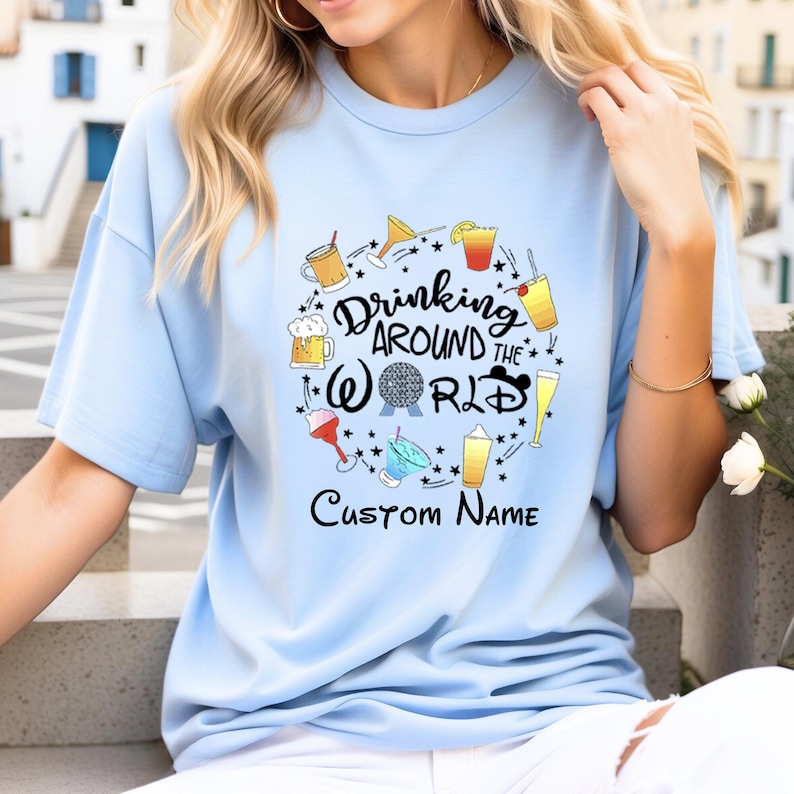 May include: Light blue t-shirt with a graphic of drinks and the text "Drinking Around the World" with a Disney World logo and the text "Custom Name".