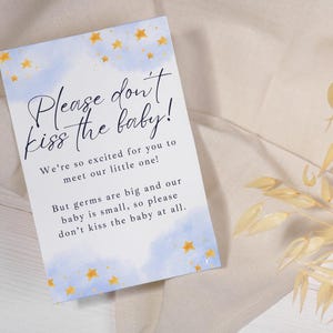Può includere: Un biglietto blu e bianco con stelle dorate stampate su di esso. Il biglietto recita "Per favore, non baciare il bambino! Siamo così emozionati che tu incontri il nostro piccolo! Ma i germi sono grandi e il nostro bambino è piccolo, quindi per favore, non baciare il bambino affatto."