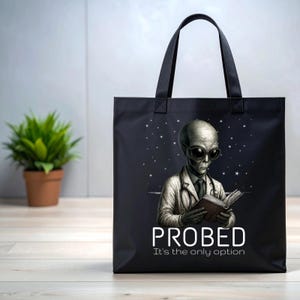 May include: Black tote bag with an illustration of an alien in sunglasses and a lab coat, reading a book. The text "PROBED It's the only option" is printed below the alien. The bag has black handles.