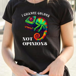 May include: Black t-shirt featuring a colorful chameleon illustration perched on a branch. The design includes the text "I Change Colors Not Opinions" in white, with the chameleon showcasing vibrant hues of green, red, and orange.