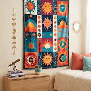 May include: A rectangular wall tapestry featuring a grid of colorful celestial illustrations including suns, moons, and stars in shades of orange, blue, red, and yellow. The design is bordered by a dark blue frame with a repeating pattern of small stars.