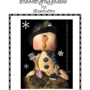 Op de afbeelding: Een handgemaakte ragdoll-sneeuwpop met een wortelneus, die een zwarte hoed, een gestreepte sjaal draagt en een schop en een bordje vasthoudt met de tekst "Ik hou van winter".