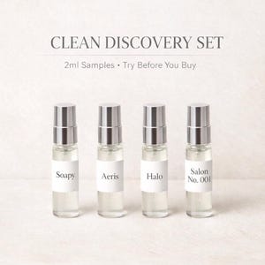 May include: A Clean Discovery Set featuring four small perfume sample bottles. Each clear glass bottle has a silver cap and a white label with a fragrance name: Soapy, Aeris, Halo, and Salon No. 001. The text "CLEAN DISCOVERY SET" is at the top.