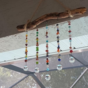 May include: A decorative wind chime featuring strands of colorful beads and crystal spheres suspended from a natural wooden branch. The beads are in various colors, including red, orange, green, and blue.