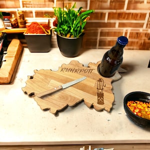 Könnte beinhalten: Ein Holzbrett in Form des Ruhrgebiets in Deutschland. Das Brett hat ein Messer, einen Flaschenhalter und den Text "RUHRPOT" eingraviert.
