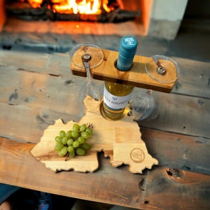 Könnte beinhalten: Holzserviertablett in Form eines Bundesstaates mit einer Flasche Weißwein und zwei Weingläsern in einem Halter. Ein Bund grüner Trauben liegt auf dem Tablett.