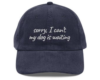 May include: Navy blue corduroy baseball cap with a curved brim. The cap features the embroidered text "sorry, I can't my dog is waiting" in white, centered on the front. The hat has a six-panel design and an adjustable strap.