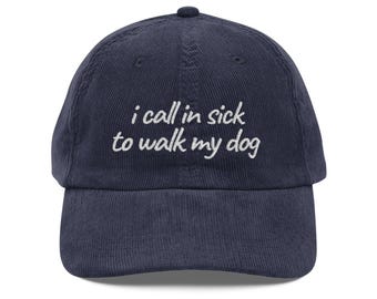 May include: Navy blue corduroy baseball cap with a curved brim. The cap features white embroidered text that reads "i call in sick to walk my dog". The cap has a rounded top and an adjustable strap.