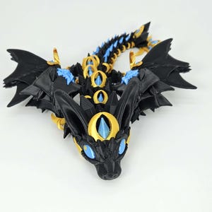 May include: A detailed, 3D-printed dragon figurine. The dragon features black, gold, and blue accents, with intricate wing and scale details. The eyes and other details are blue. The dragon is a fantasy-themed item.