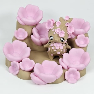 May include: A 3D-printed figurine of a cartoon-like creature with a tree-like head, adorned with pink flowers. The figurine stands in a tan-colored landscape surrounded by large pink flowers. The overall design is whimsical and decorative.