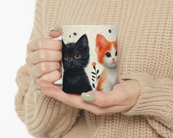 May include: White ceramic mug with a black and orange cat illustration. The cats are looking at the viewer and are surrounded by small flowers and leaves.