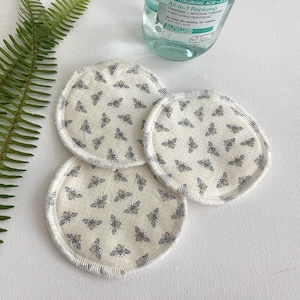 May include: Three white reusable makeup remover pads with a bee pattern. The pads have a white border and are made of soft fabric.