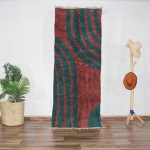 Peut inclure: Un tapis rectangulaire long avec un motif géométrique de lignes courbes dans des tons de bleu sarcelle et rouille. Le tapis a une texture douce et duveteuse.