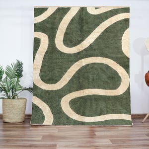 May include: A green and cream abstract area rug with a wavy, organic pattern. The rug has a soft, plush texture.