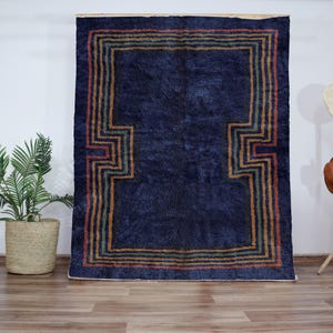 May include: A dark blue rug with a multi-colored geometric pattern border. The rug has a distressed, vintage look.