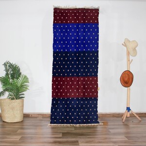 Peut inclure: Un tapis long et étroit avec un motif répétitif de petits points blancs sur un fond bleu foncé. Le tapis est divisé en quatre bandes horizontales, les bandes supérieure et inférieure étant de couleur rouge foncé et les deux bandes du milieu étant de couleur bleu foncé.