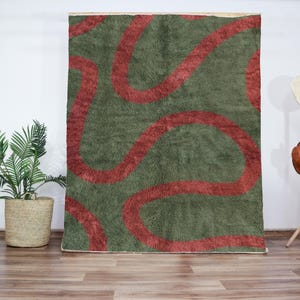 Peut inclure: Un tapis abstrait vert et rouge avec un motif ondulé. Le tapis est fait d'un matériau doux et moelleux.