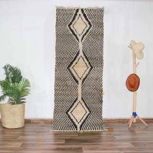 Peut inclure: Un tapis marocain noir et blanc avec un motif en losange. Le tapis est en laine et a des franges aux extrémités.
